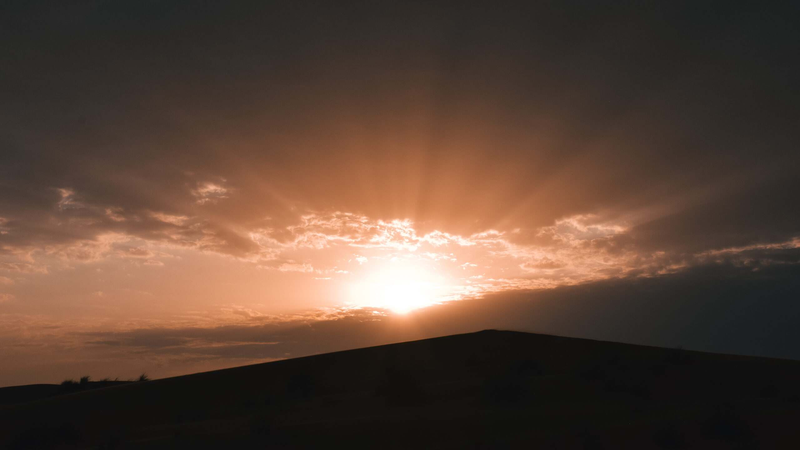 Epic desert sunset over the rolling sand dunes of Wahiba Sands in Oman, with the golden sun setting on the horizon